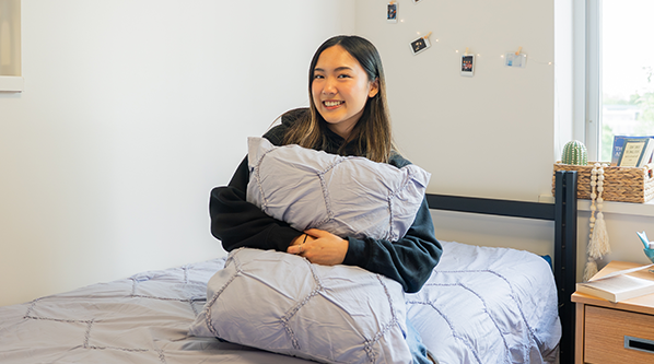 Student sitting on a bed holding a pillow